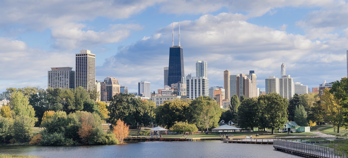 A serene view of Lincoln Park in Chicago, featuring lush greenery, a tranquil pond, and the skyline in the distance, with Lincoln Park Zoo nearby