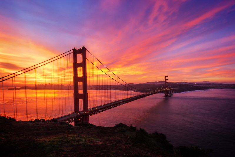 A stunning view of the Golden Gate Bridge at sunrise, with the orange structure standing out against a misty bay backdrop.